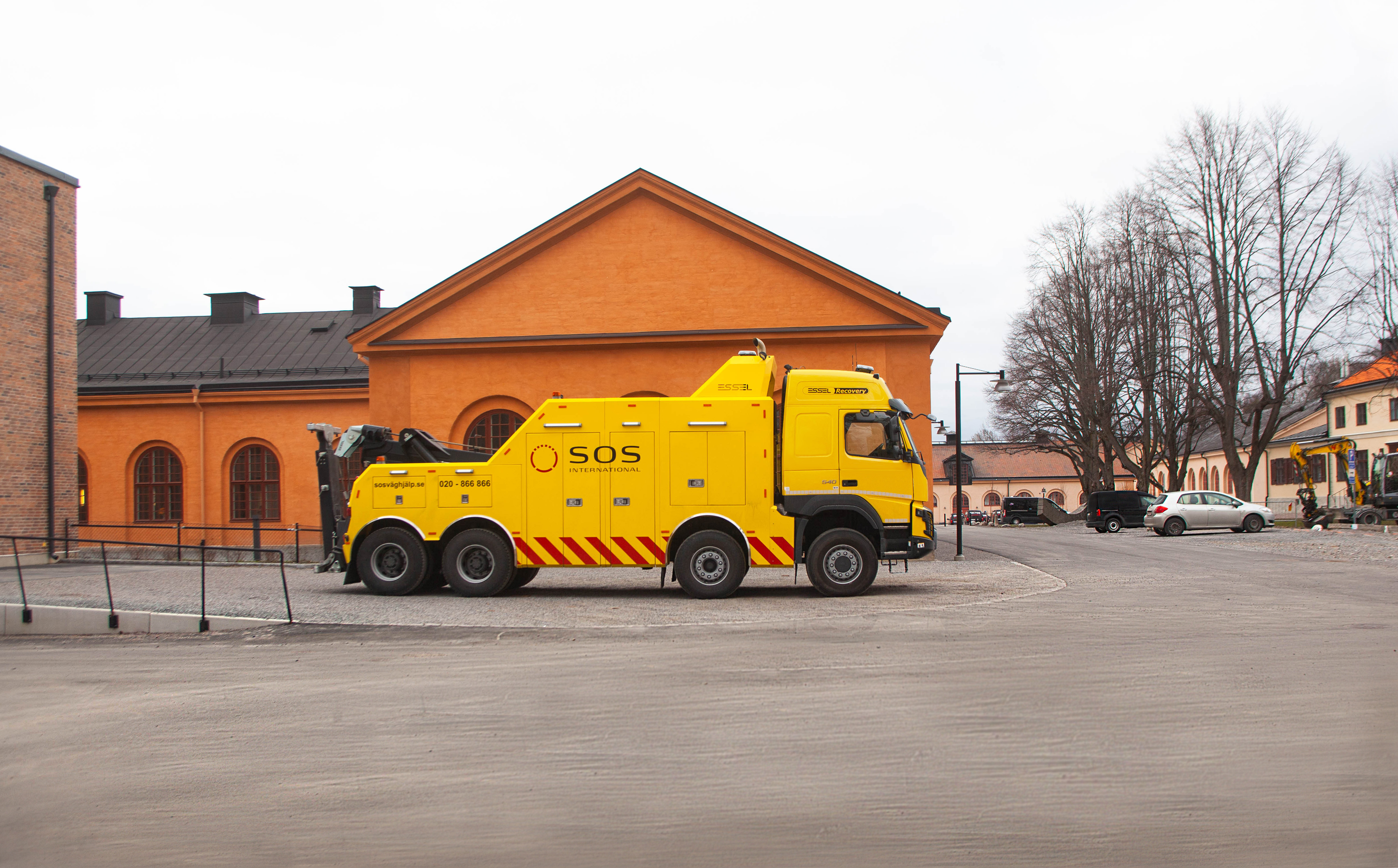 En gul bärgningslastbil parkerad framför ett orange hus.