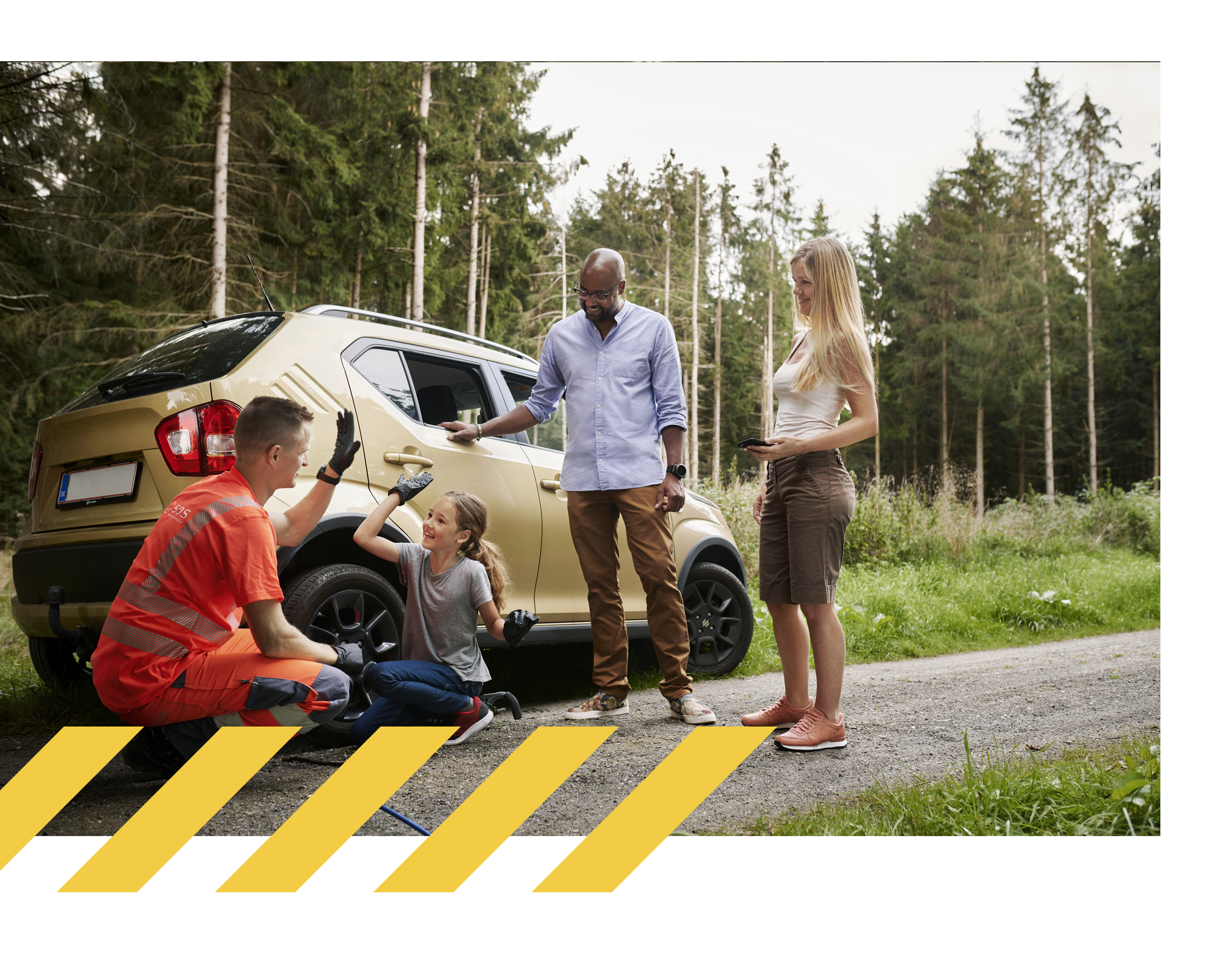 En bärgningsarbetare gör en high five med en flicka framför en parkerad guldfärgad bil på en skogsväg, medan en man och en kvinna står bredvid och ler.