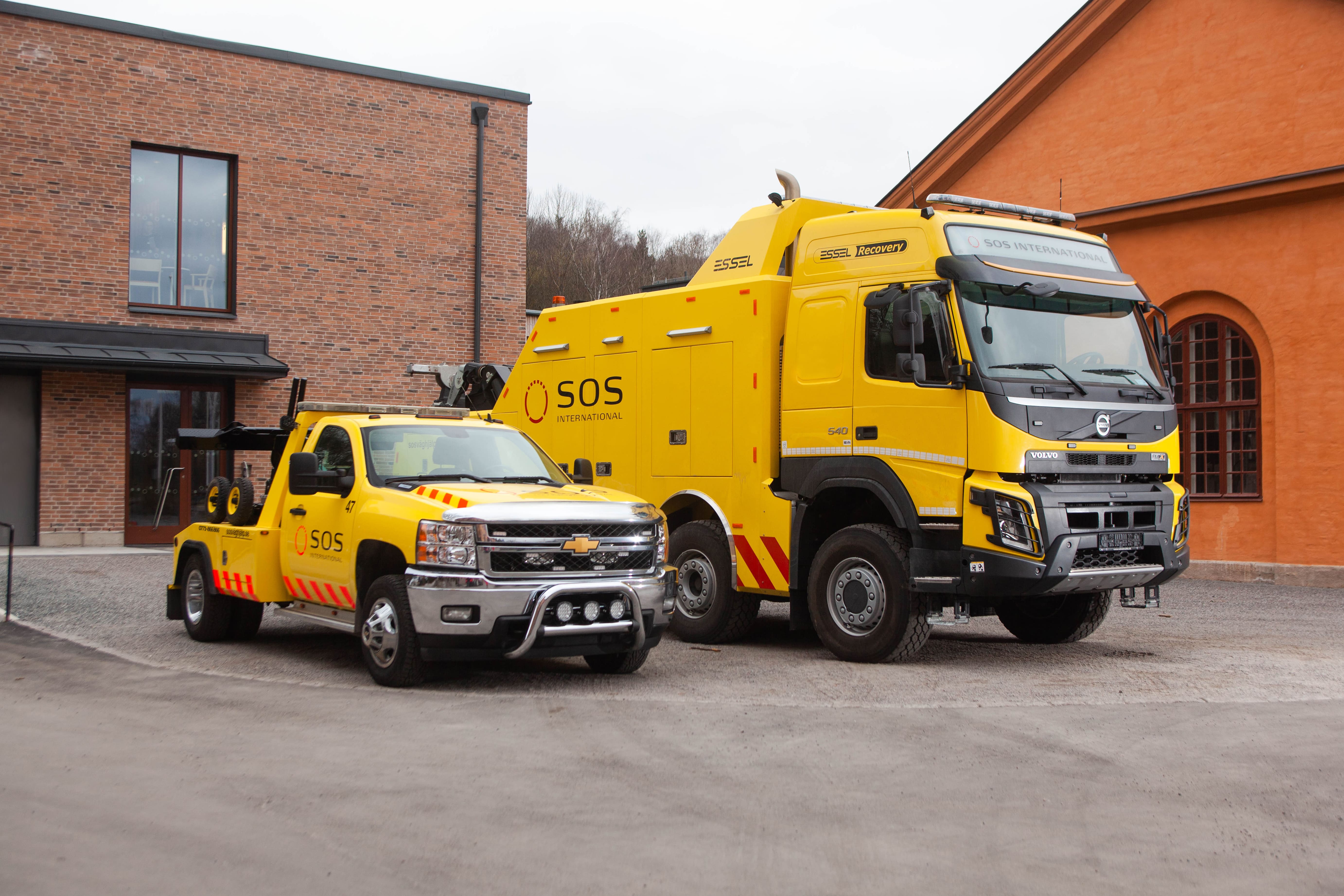 Två gula bärgningsfordon parkerade på rad, med en vanlig bärgningsbil till vänster och en bärgningslastbil till höger.