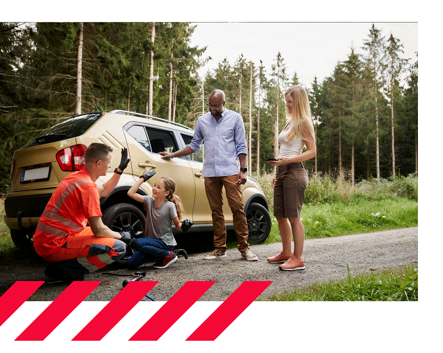 En bärgningsarbetare gör en high five med en flicka framför en parkerad guldfärgad bil på en skogsväg, medan en man och en kvinna står bredvid och ler.